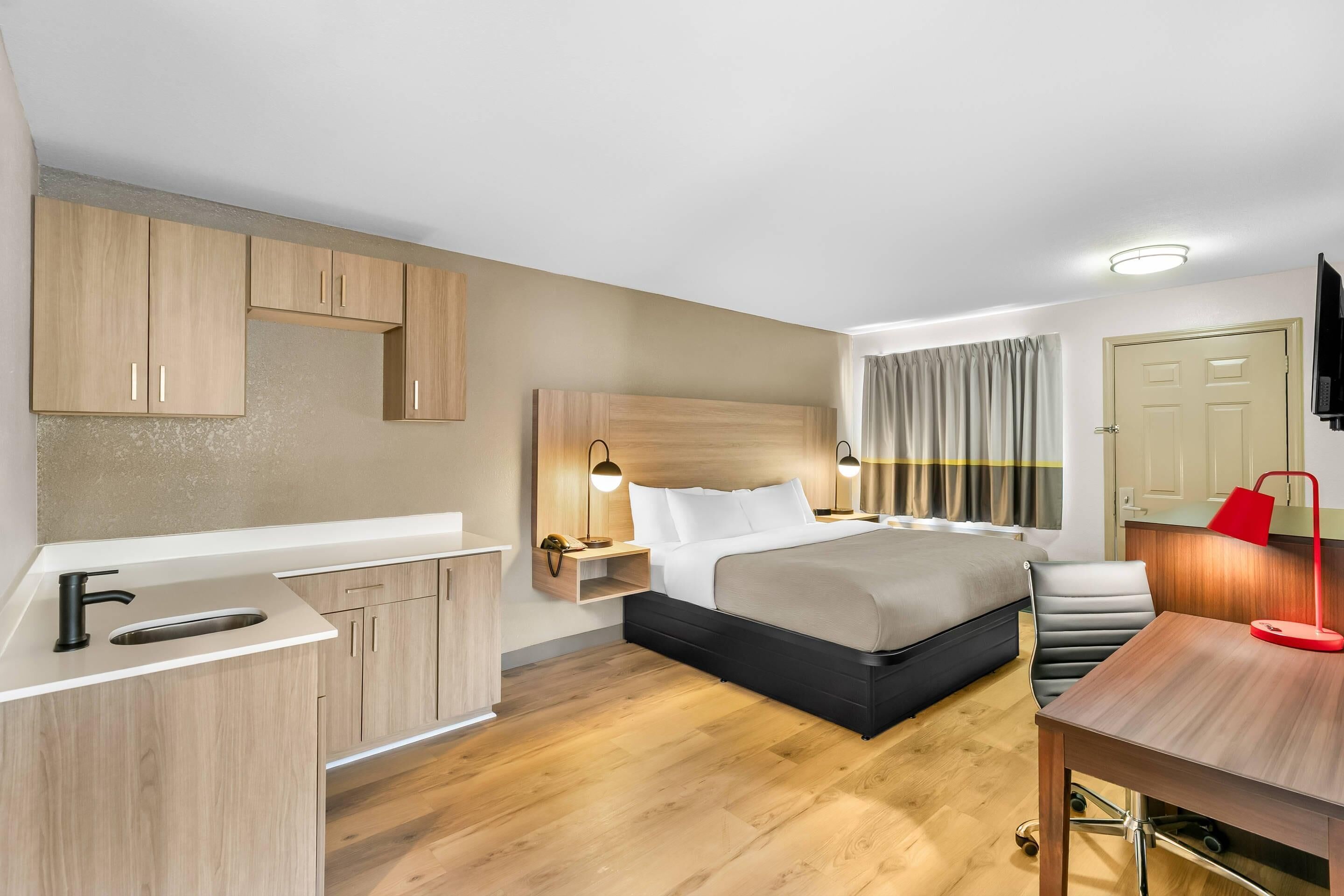 A hotel room with a bed, bedside table, desk, and a TV mounted on the wall.