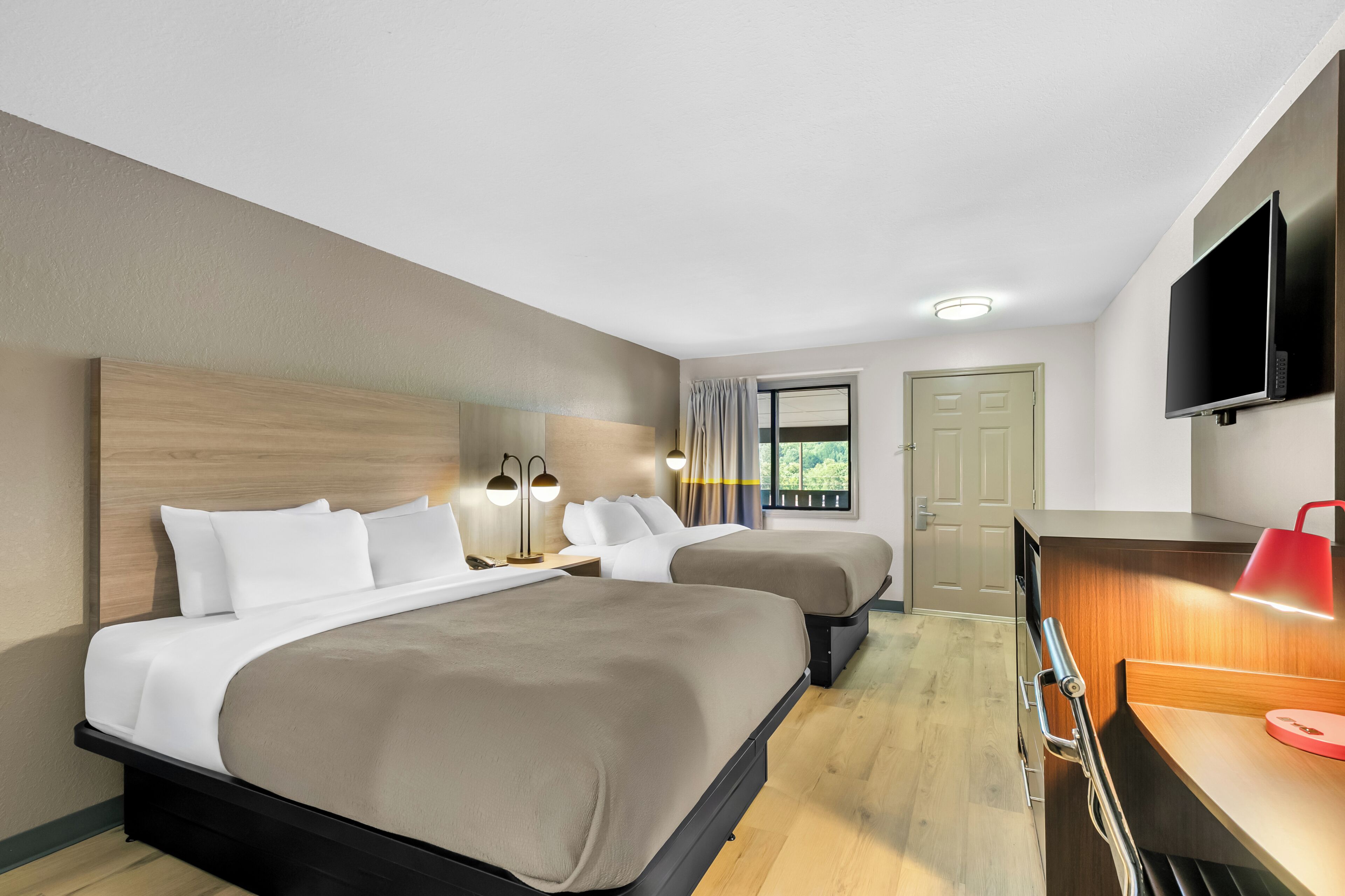 A hotel room with two beds, a desk, a TV, and a window with curtains.