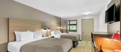 A hotel room with two beds, a desk, a TV, and a window with curtains.