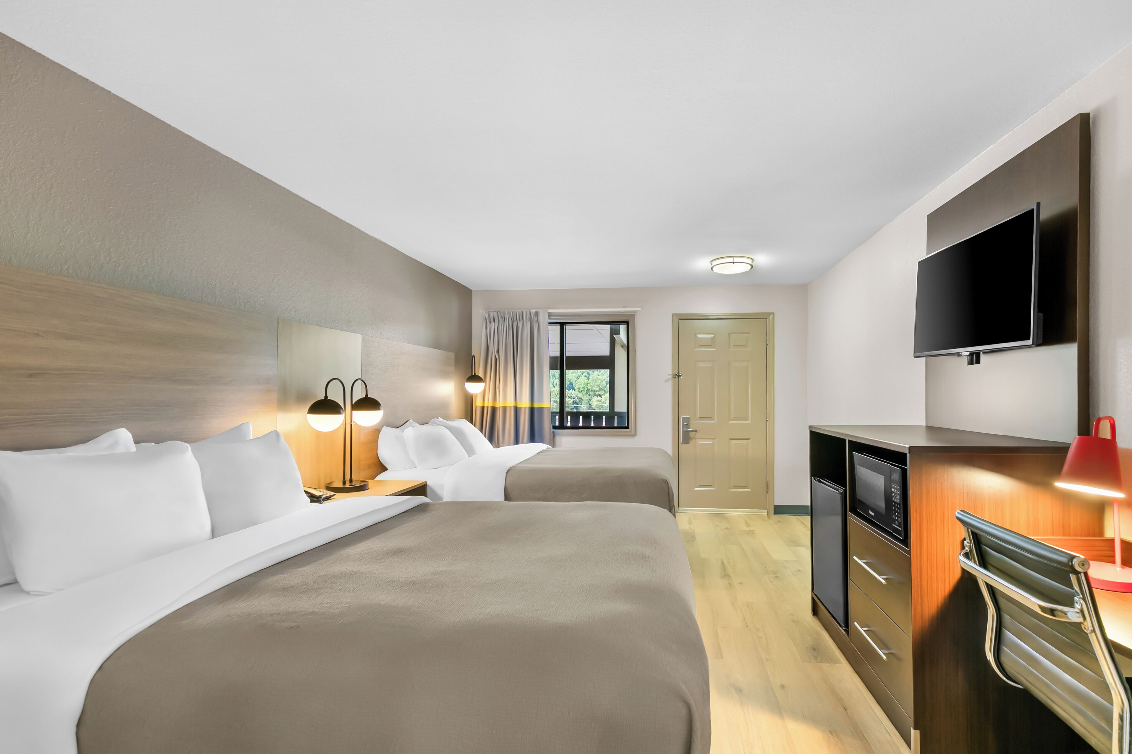A hotel room with two beds, a TV, a desk with a microwave, and a door leading to a balcony.