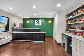 A hotel reception area with a green wall, a reception desk, and a snack bar with various packaged goods. - Quality Inn (Helen)