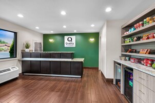 Zona de recepción de hotel con una pared verde, un mostrador de recepción y un bar de aperitivos con diversos productos envasados.