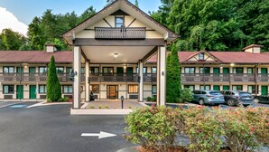 Ein Hotel mit überdachter Eingangspartie, mehreren Balkonen und einem Parkplatz.
