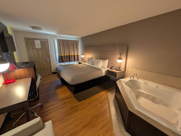 Habitación de hotel con cama, escritorio con lámpara, teléfono, ventana con cortinas y bañera.