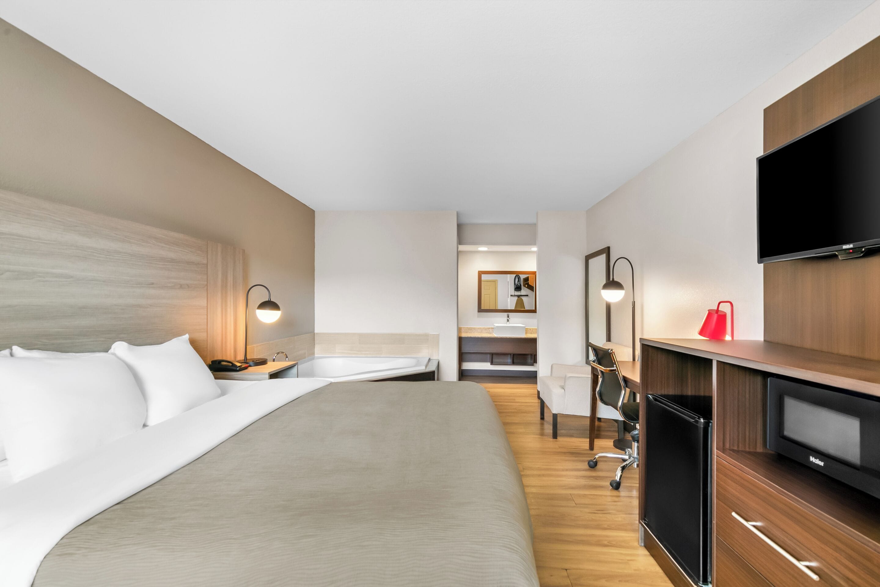 Habitación de hotel con cama, escritorio, silla, televisor y baño visible a través de una puerta abierta.