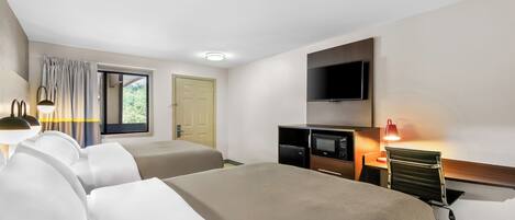 A hotel room with two beds, a flat-screen TV, a microwave, and a desk with a lamp.
