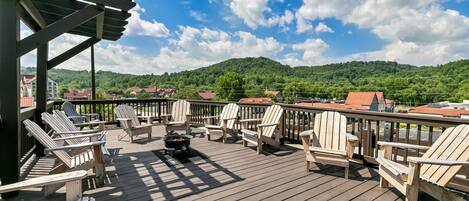 Eine Holzterrasse mit Adirondack-Stühlen und einem Feuerkorb, mit Blick auf eine Stadt und sanfte Hügel.