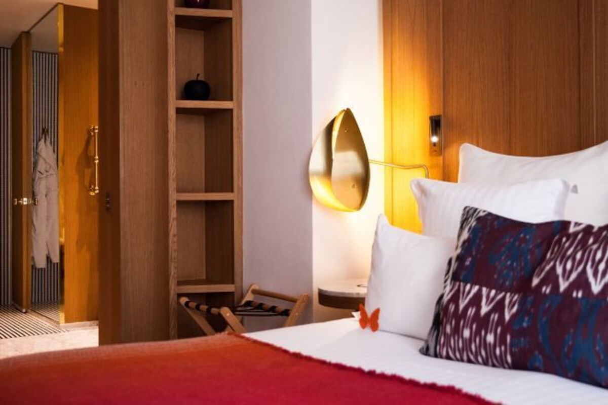 Een hotelkamer met een bed, een houten kledingkast, een plankje met een decoratie en een wandlamp.