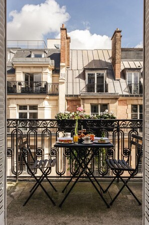 A balcony with a table set for breakfast, including a flower arrangement, a glass of orange juice, and a plate of food. - Hotel Vernet (Paris)