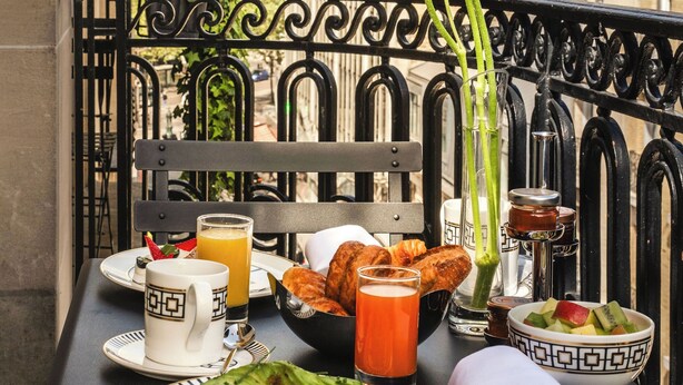 Une table avec des aliments pour le petit-déjeuner, un vase rempli de fleurs et, en arrière-plan, une vue sur la ville.