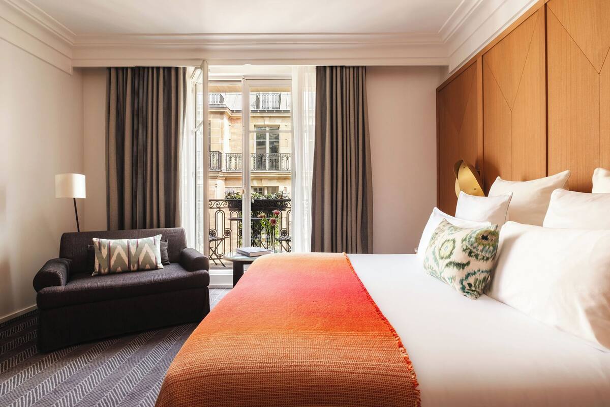 A hotel room with a bed, a sofa, a small table, and a view of the outside balcony.