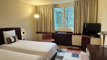 A hotel room with two beds, a desk, a TV, and a window with curtains.