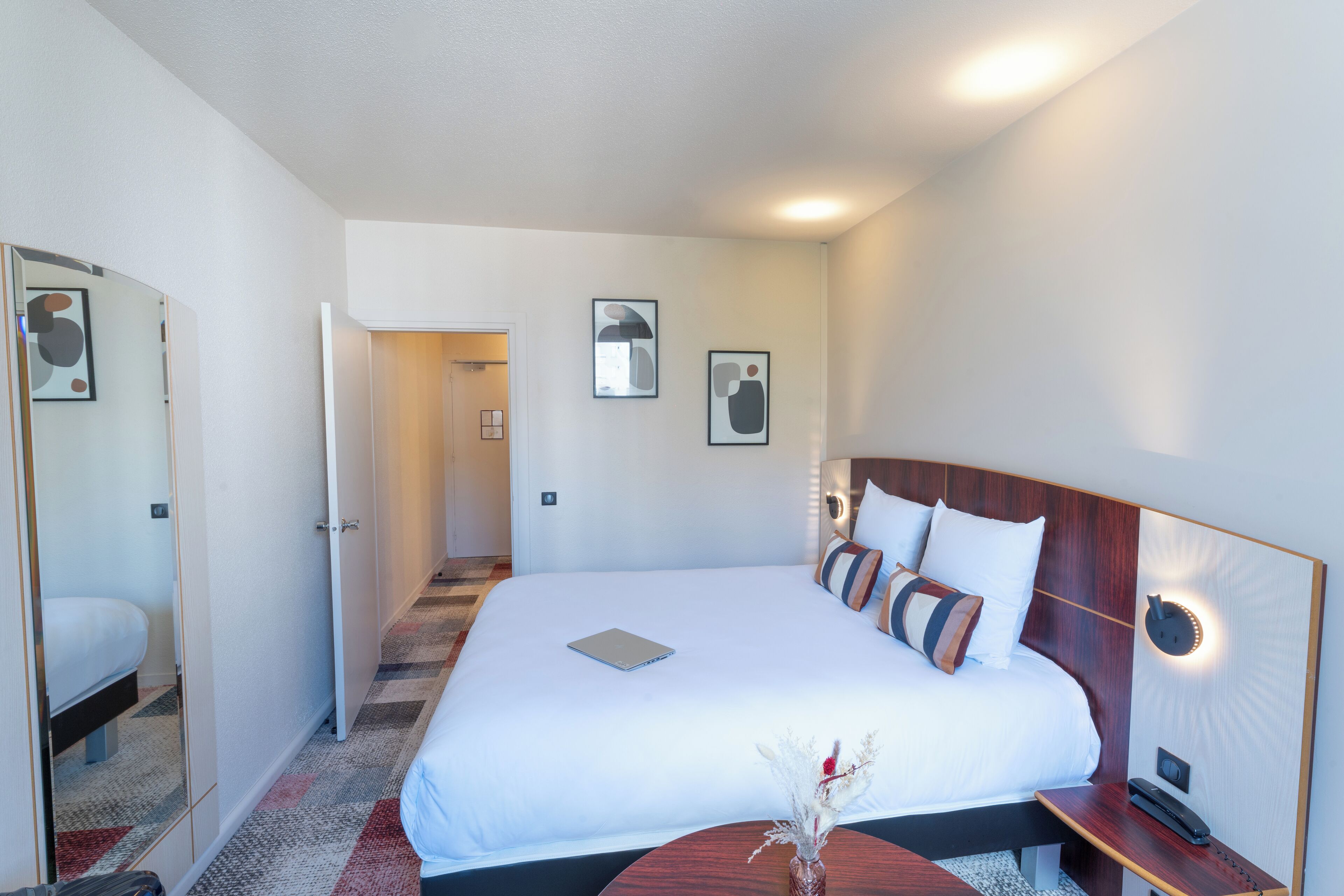Hotellihuone, jossa on suuri sänky, yöpöytä ja peili.