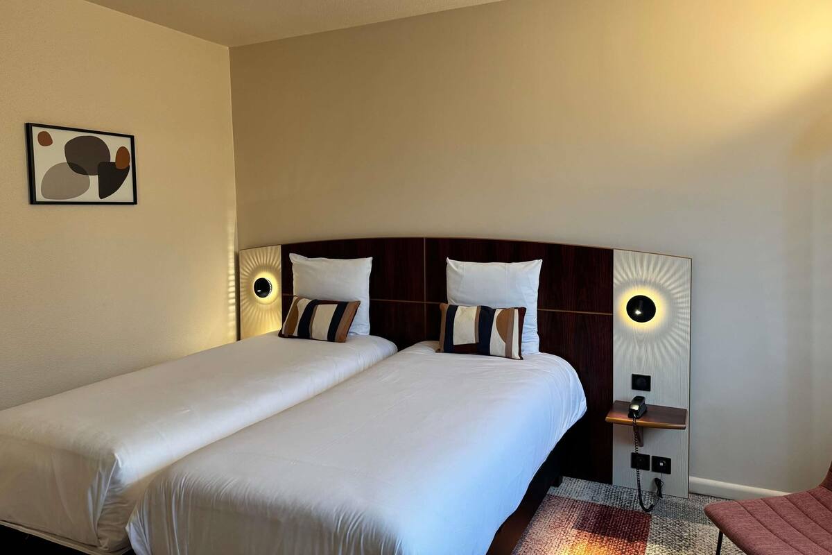 A double bed with white linens, a wooden headboard, and two bedside lamps.