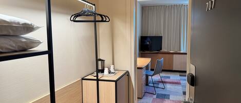 Habitación de hotel con literas, un escritorio con tetera, una silla y un televisor en la esquina.