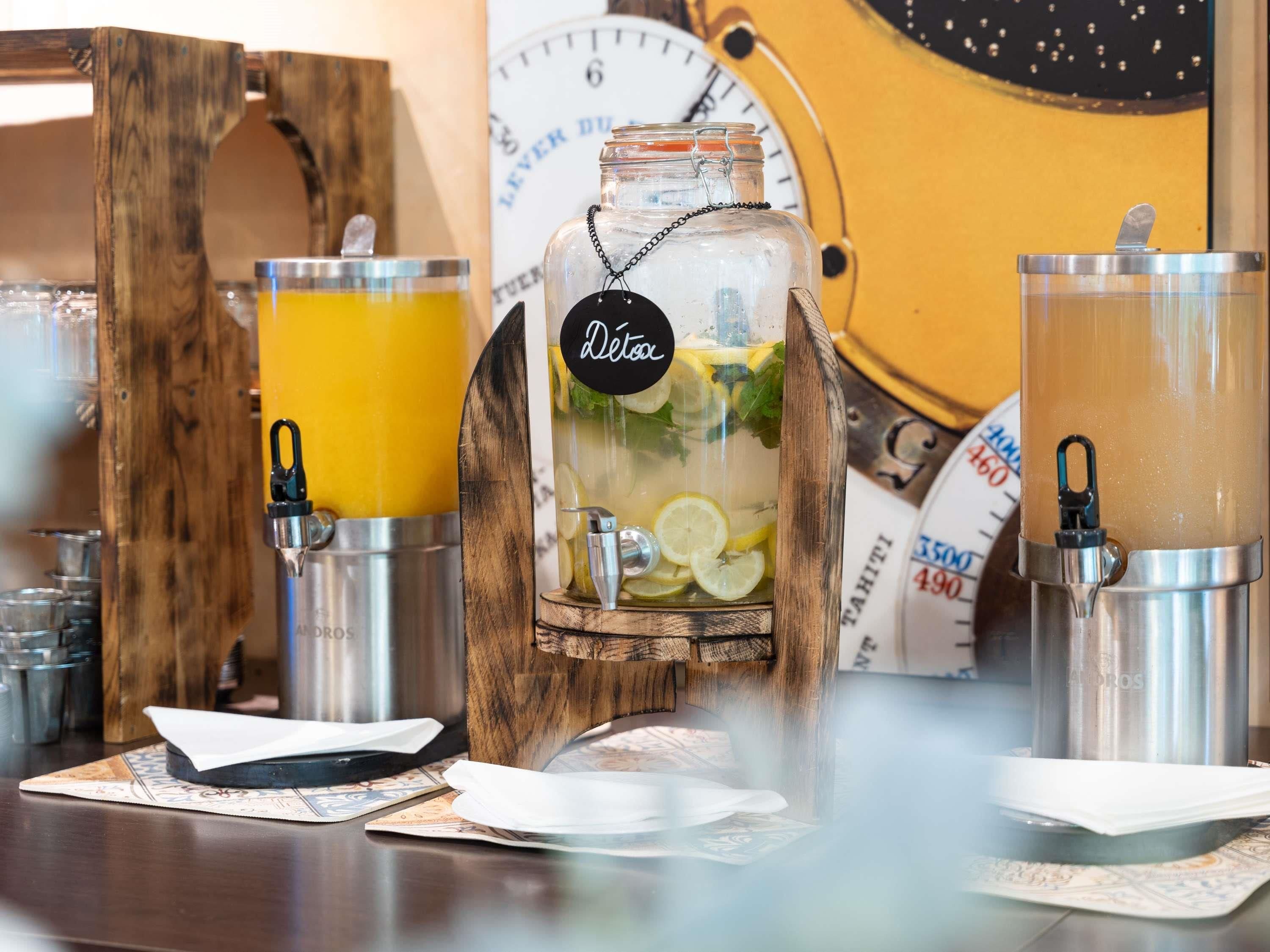 A bar area with a wooden bar counter, a glass jar with a label, and two metal dispensers with drinks.