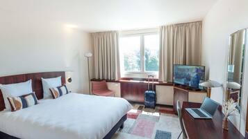 A hotel room with a bed, a desk with a laptop, a television, and a suitcase.