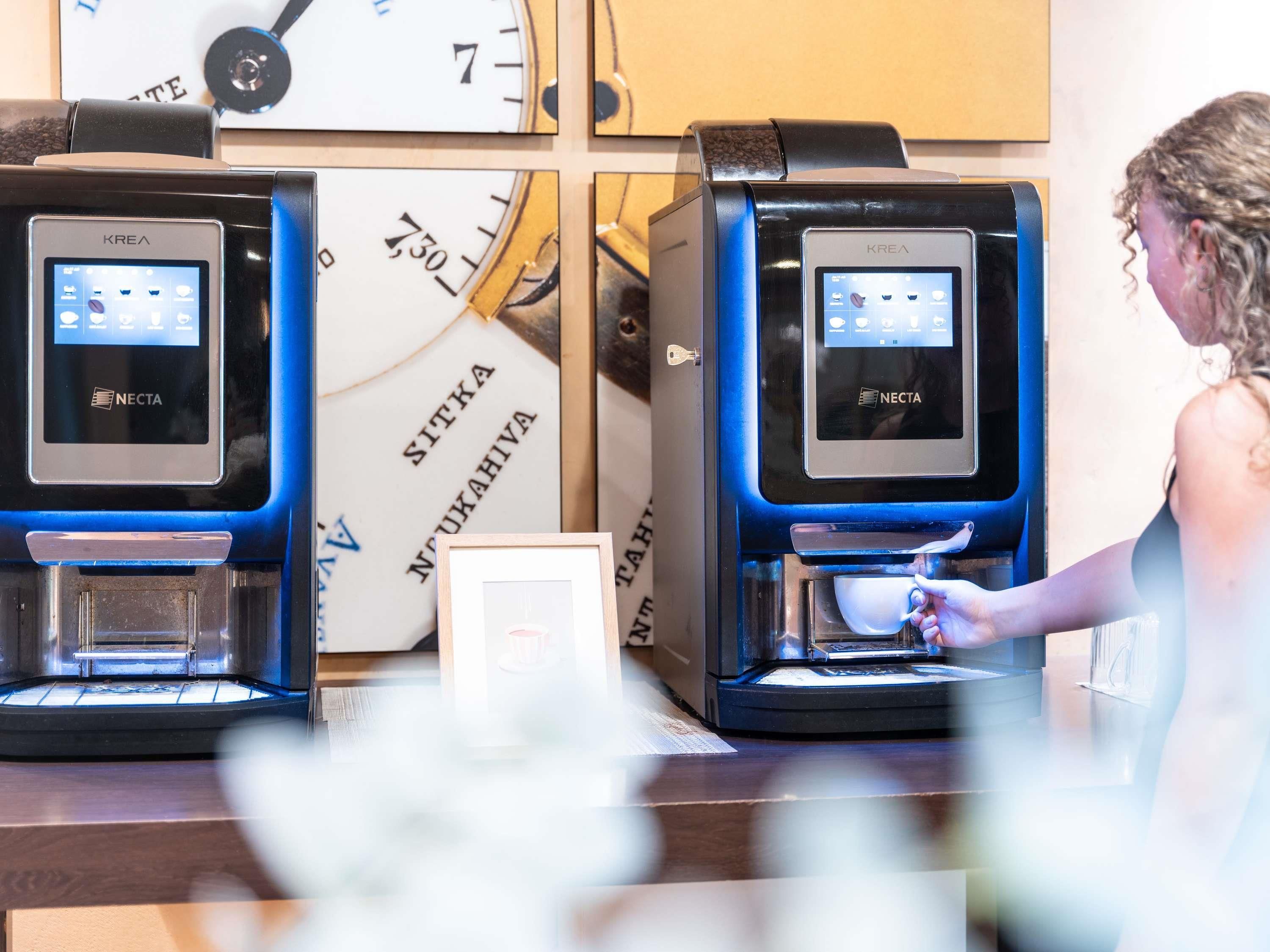 A coffee machine with a digital interface, a wall clock, and a framed picture on a counter.