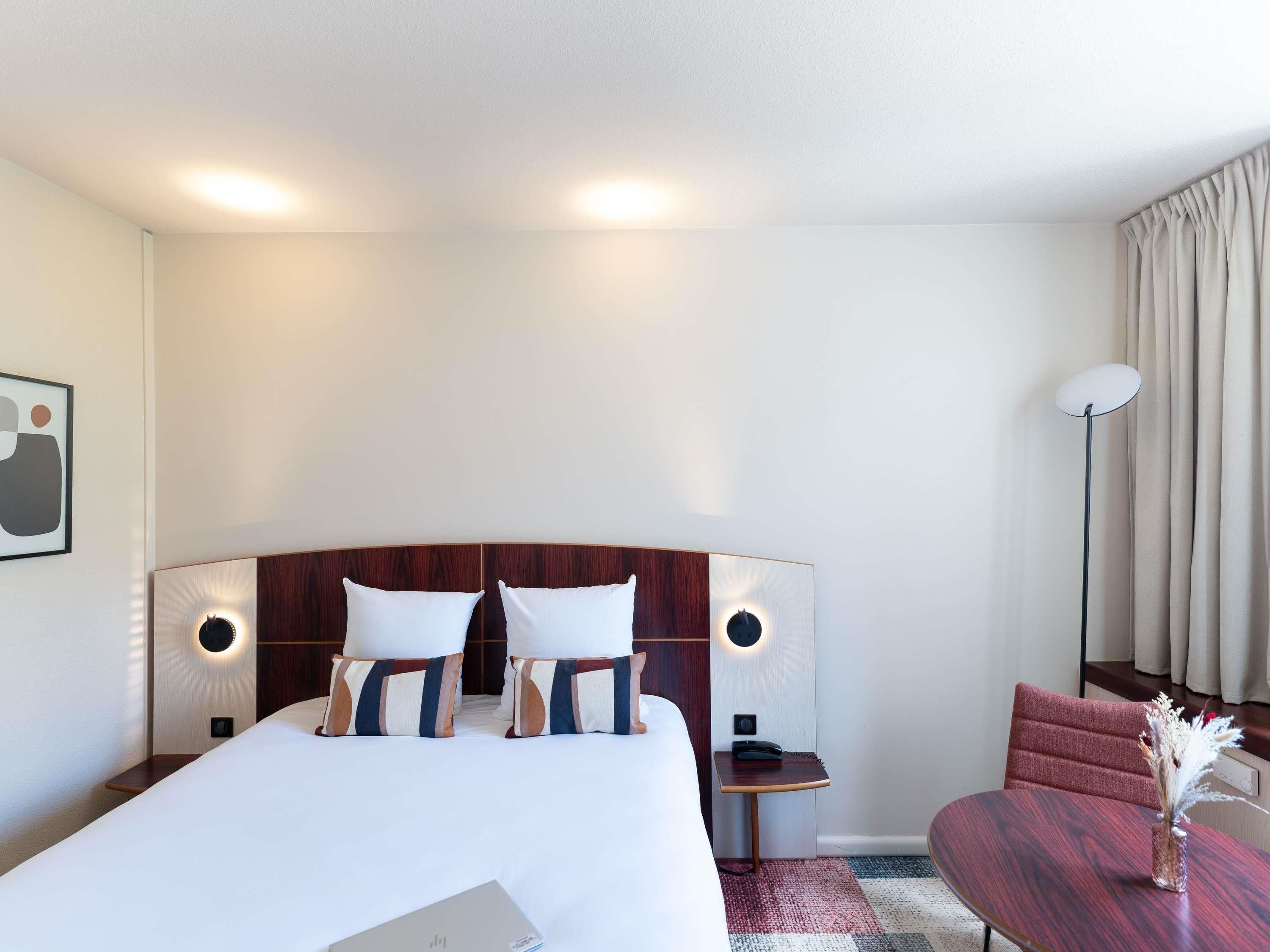 Una habitación de hotel con una cama grande, mesitas de noche, un escritorio, una silla y una lámpara de pie.