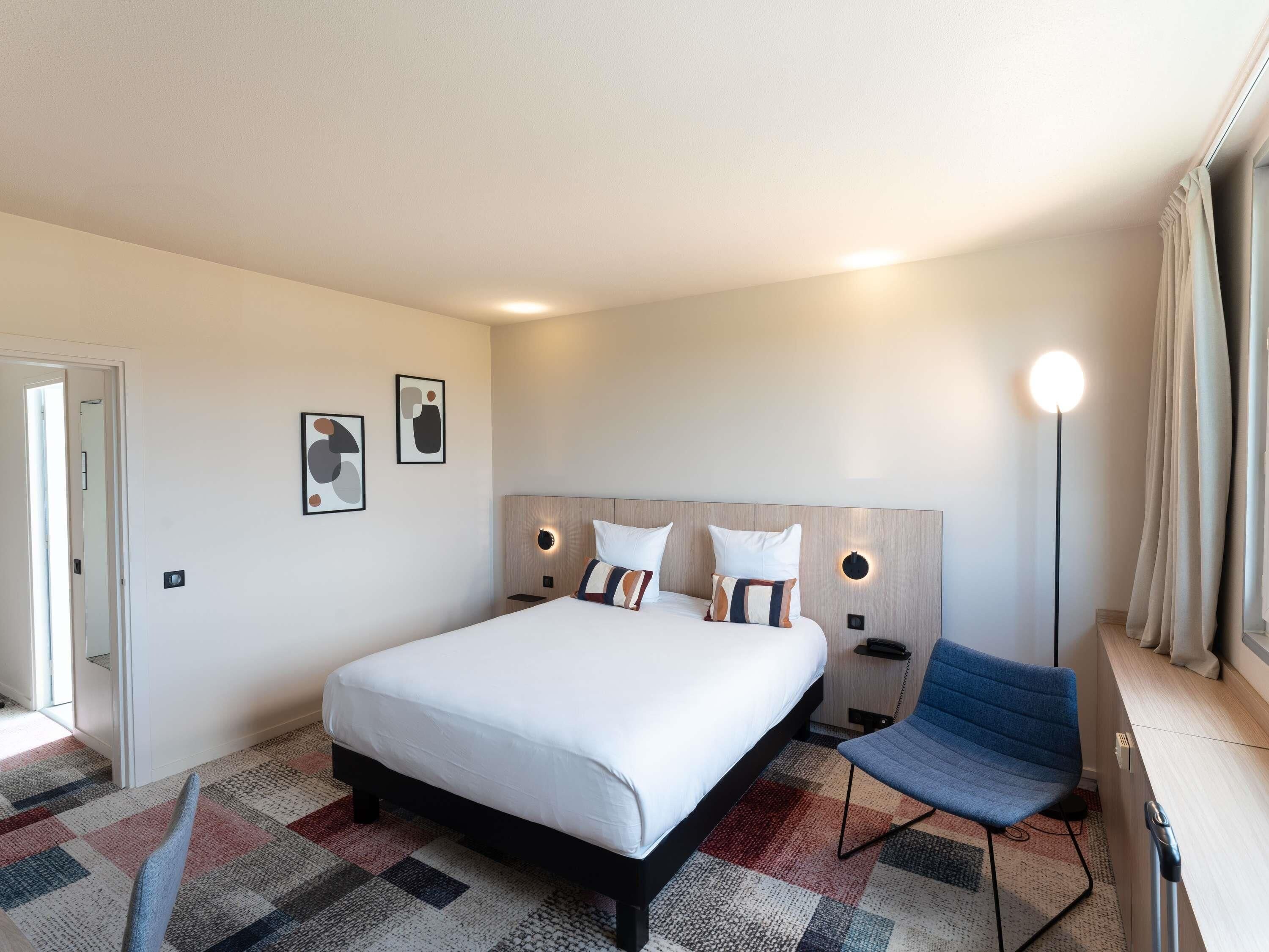 Una habitación de hotel con una cama grande, una silla, un escritorio y una lámpara.