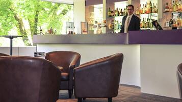 A bar area with leather chairs, a counter with various bottles, and a view of trees through large windows.