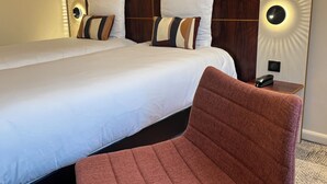 A hotel room with a large bed, two pillows, a nightstand with a phone, and a red chair.