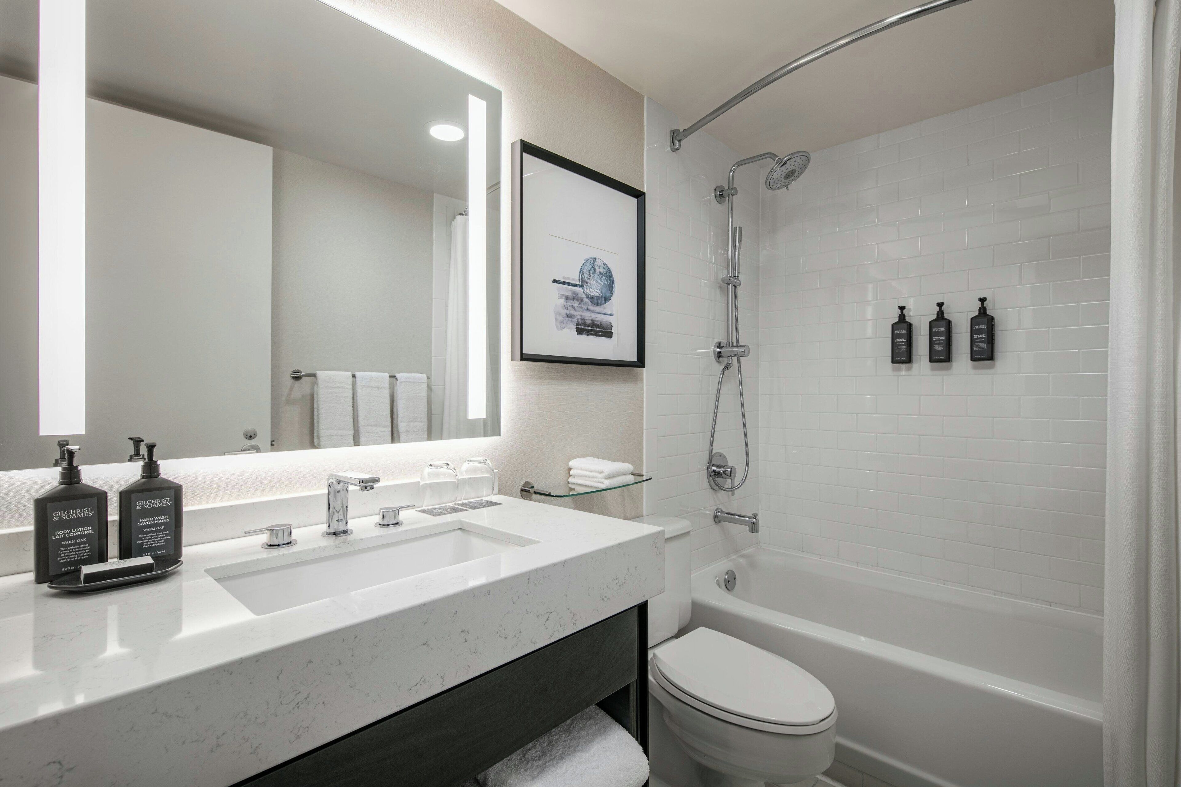A modern bathroom with a white sink, a mirror, a framed picture, and a shower.