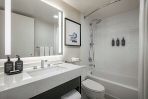 A modern bathroom with a white sink, a mirror, a framed picture, and a shower. - Sheraton LaGuardia East Hotel (Flushing)
