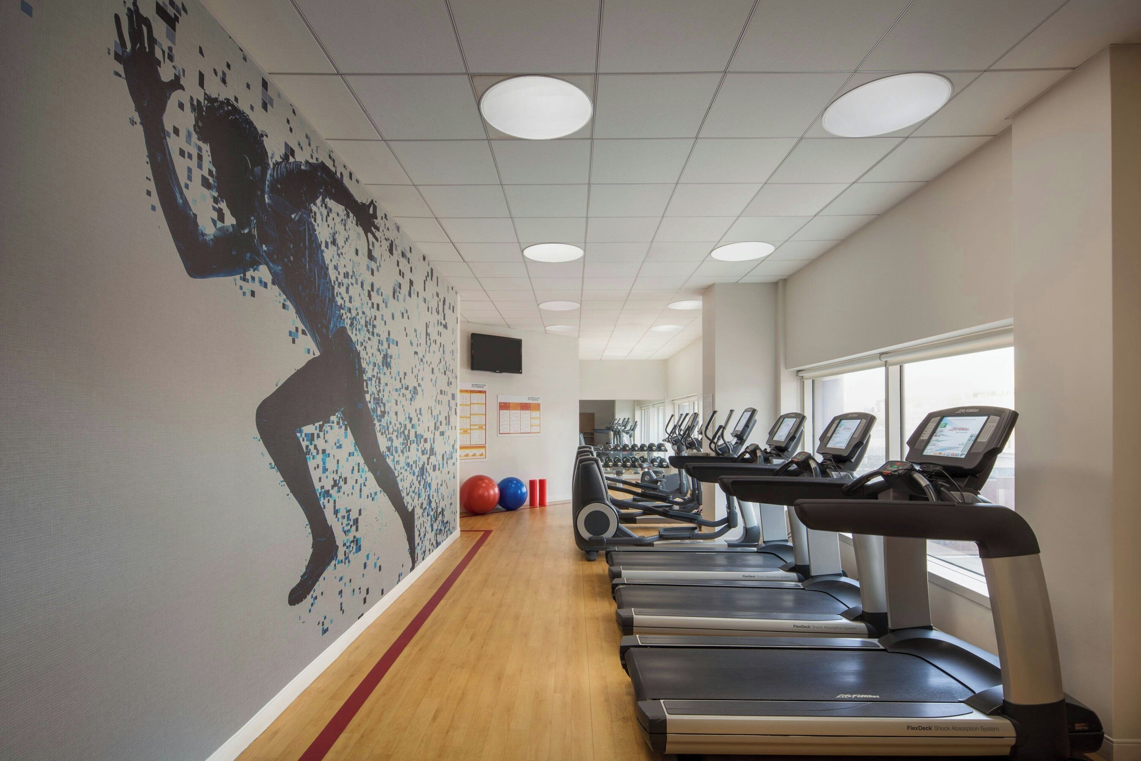 Un gimnasio con cintas de correr, pelotas de ejercicios y un mural en la pared.