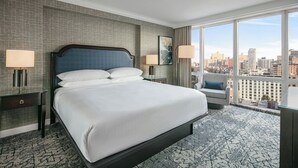 A hotel room with a large bed, two bedside tables, a chair, and a city view. - Sheraton LaGuardia East Hotel (Flushing)