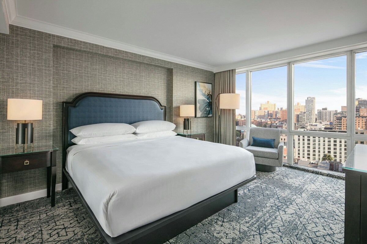 A hotel room with a large bed, two bedside tables, a chair, and a city view.