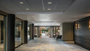 A hotel corridor with a patterned carpet, large pillars, and a patterned wall with wall sconces. - Sheraton LaGuardia East Hotel (Flushing)
