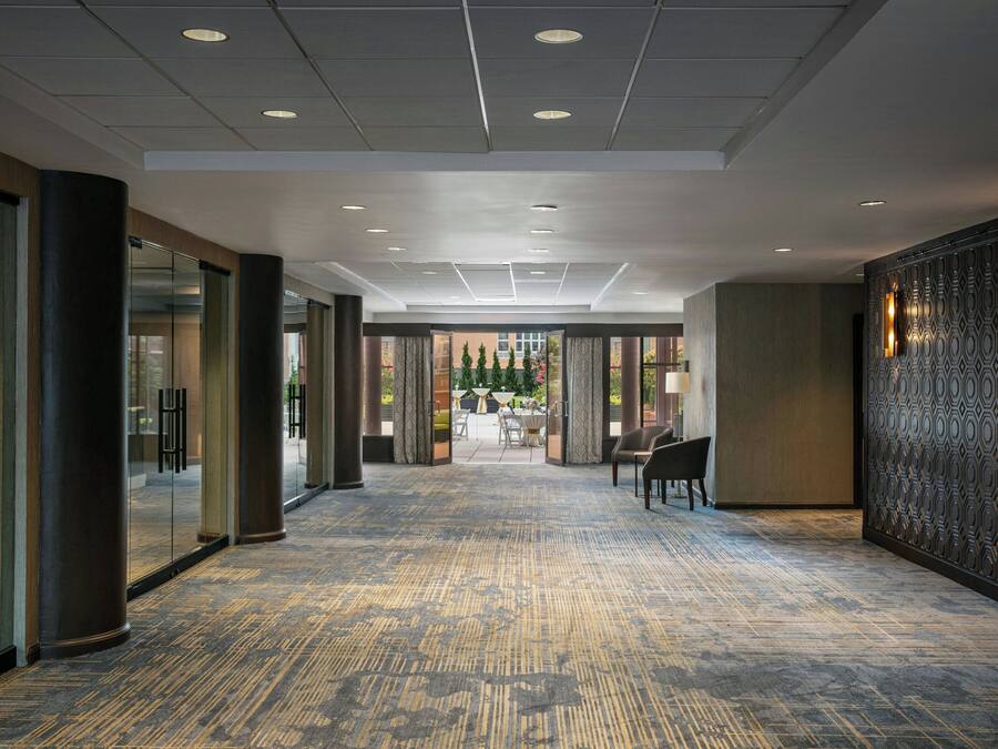 A hotel corridor with a patterned carpet, large pillars, and a patterned wall with wall sconces.