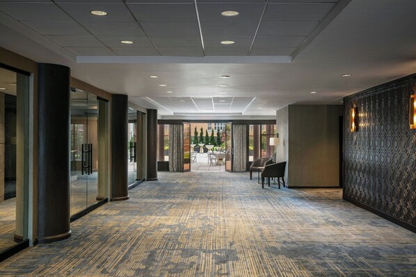 A hotel corridor with a patterned carpet, large pillars, and a patterned wall with wall sconces.