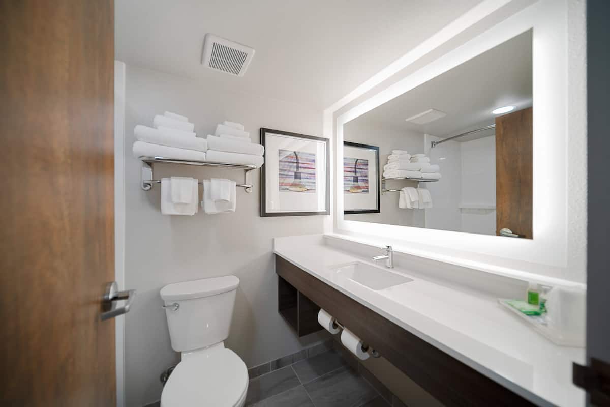 A modern bathroom with a white toilet, a large mirror, and a vanity with a sink and towel rack.