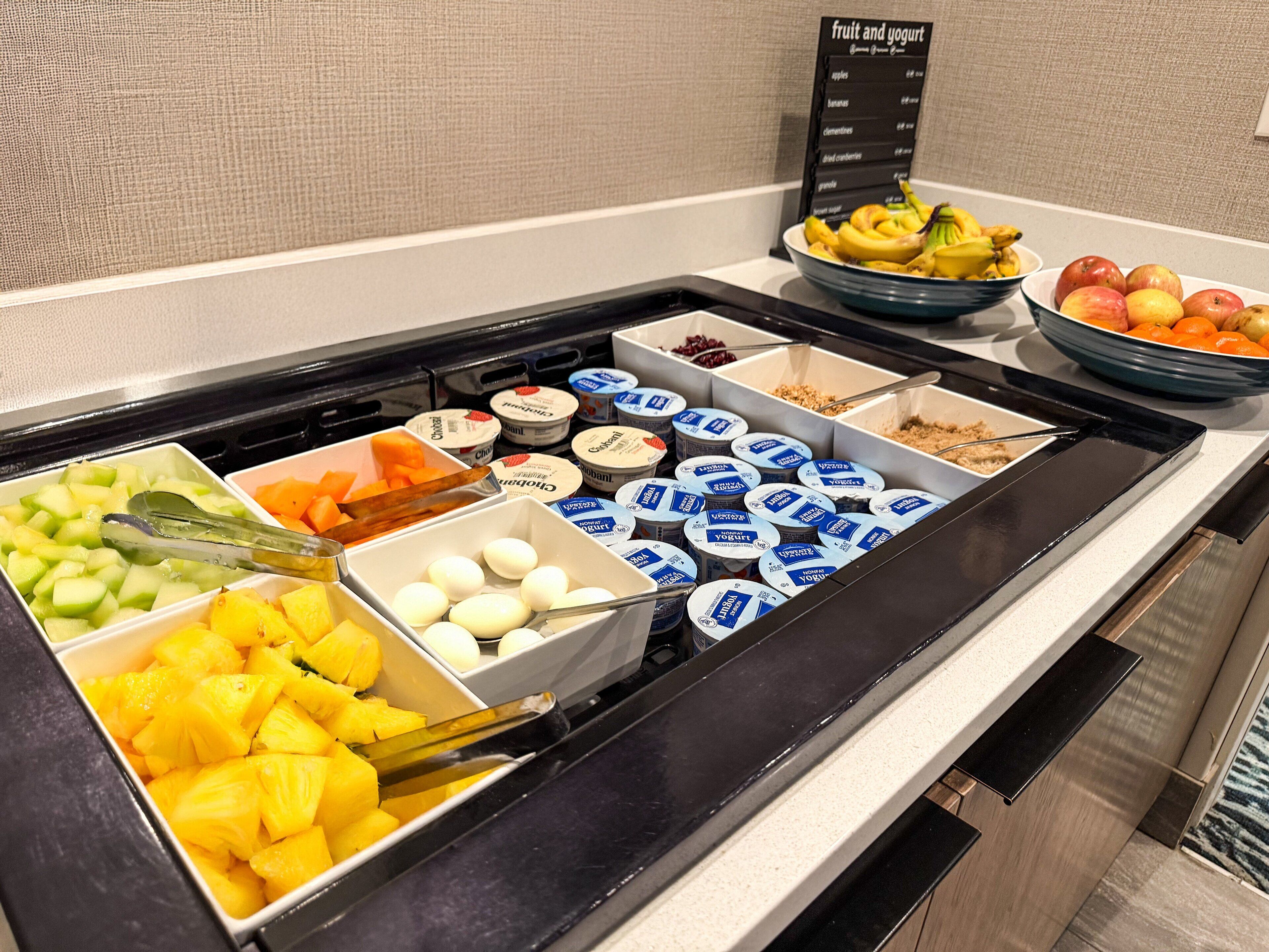 Un bufé con diversas frutas, yogur y otros alimentos.