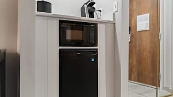 A compact kitchen with a microwave and a built-in oven, white walls, and a wooden door in the background.