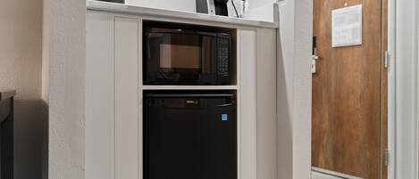 A compact kitchen with a microwave and a built-in oven, white walls, and a wooden door in the background.