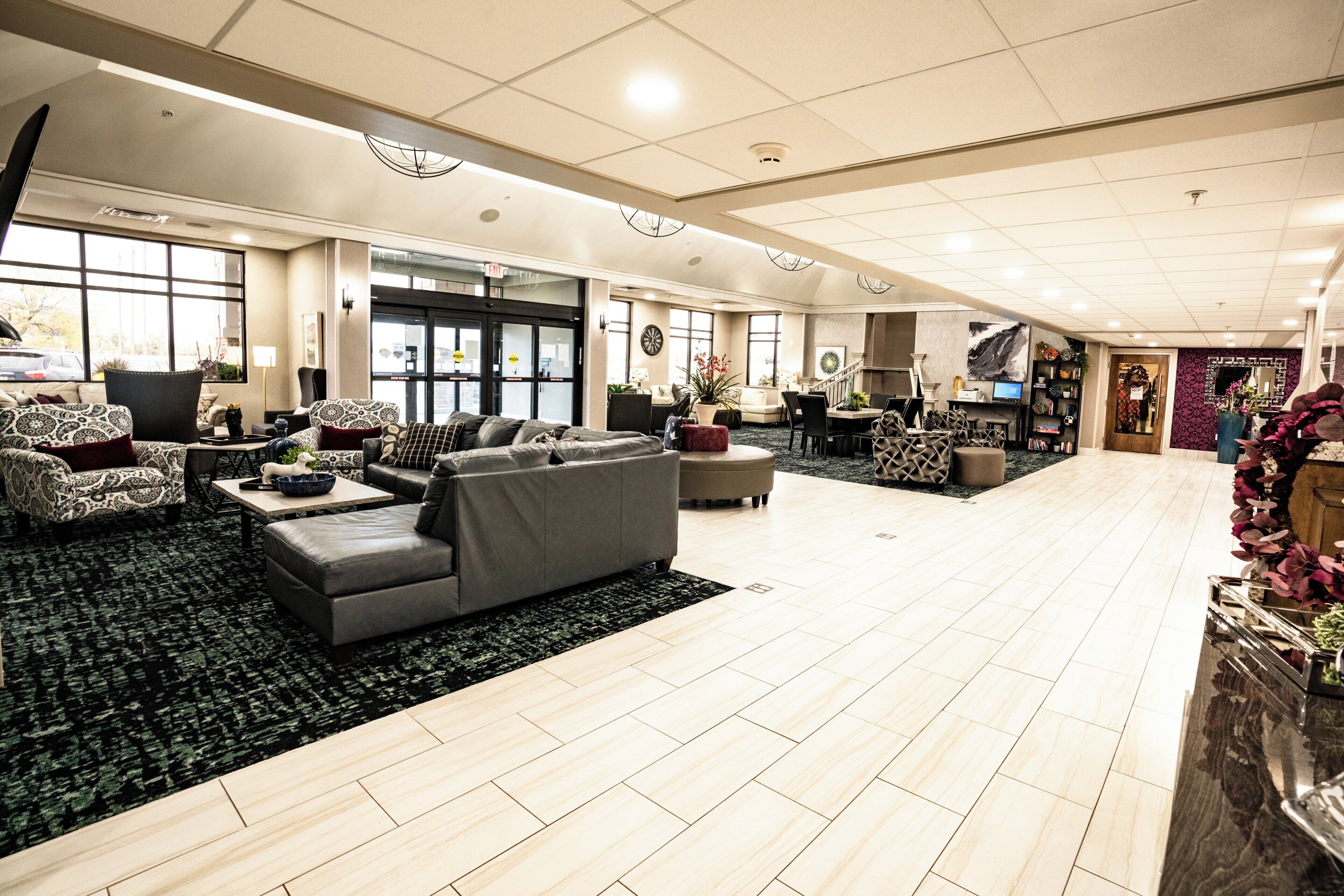 A spacious hotel lobby with a large seating area, a reception desk, and a staircase leading to upper floors.