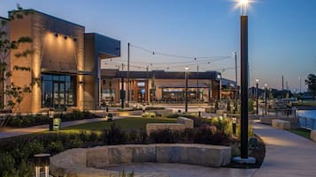 A modern building with a brick facade, outdoor seating area, and a well-lit entrance.