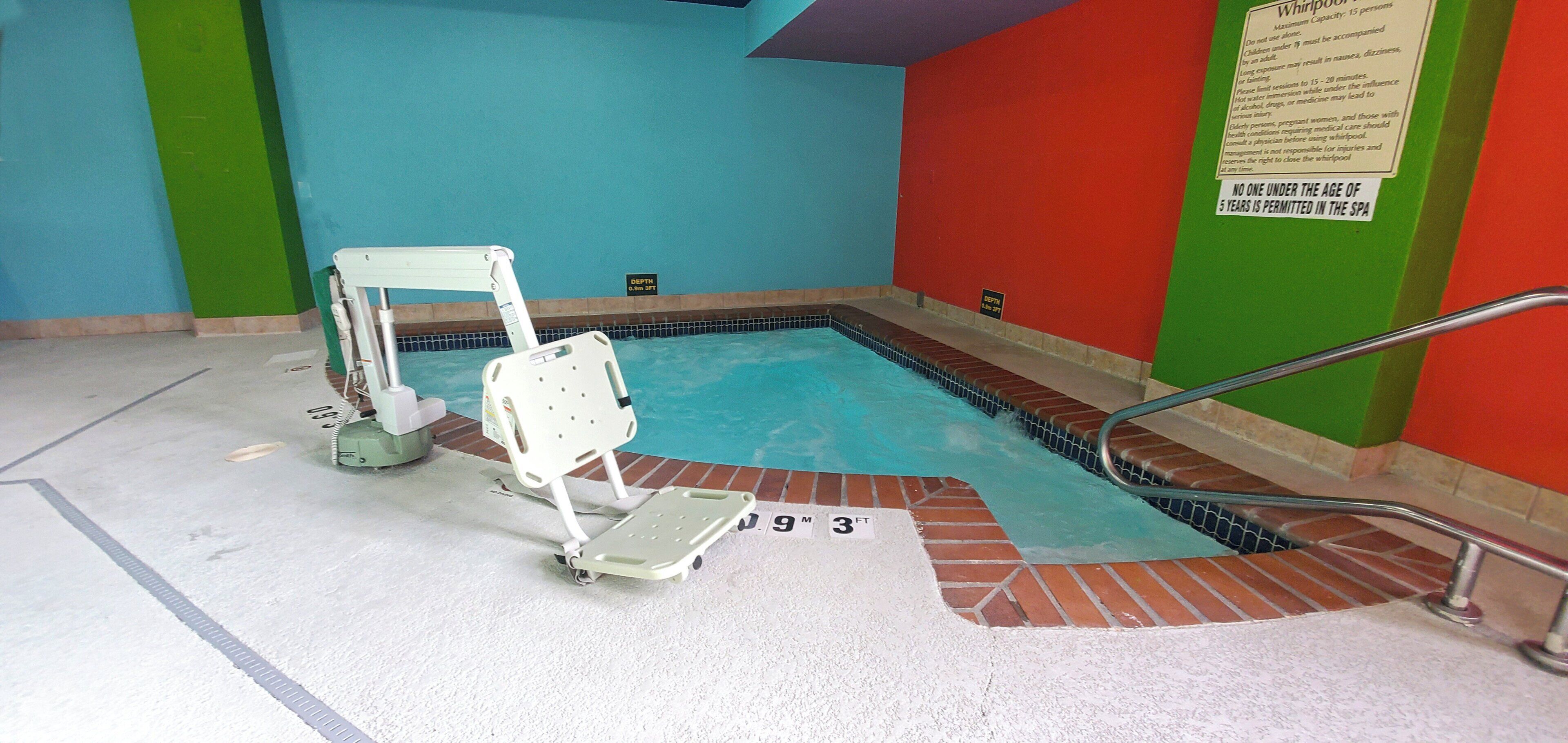 Une petite piscine intérieure dotée d’un indicateur de profondeur, d’un dispositif d’élévation pour faciliter l’accès à la piscine et d’un panneau de sécurité fixé au mur.