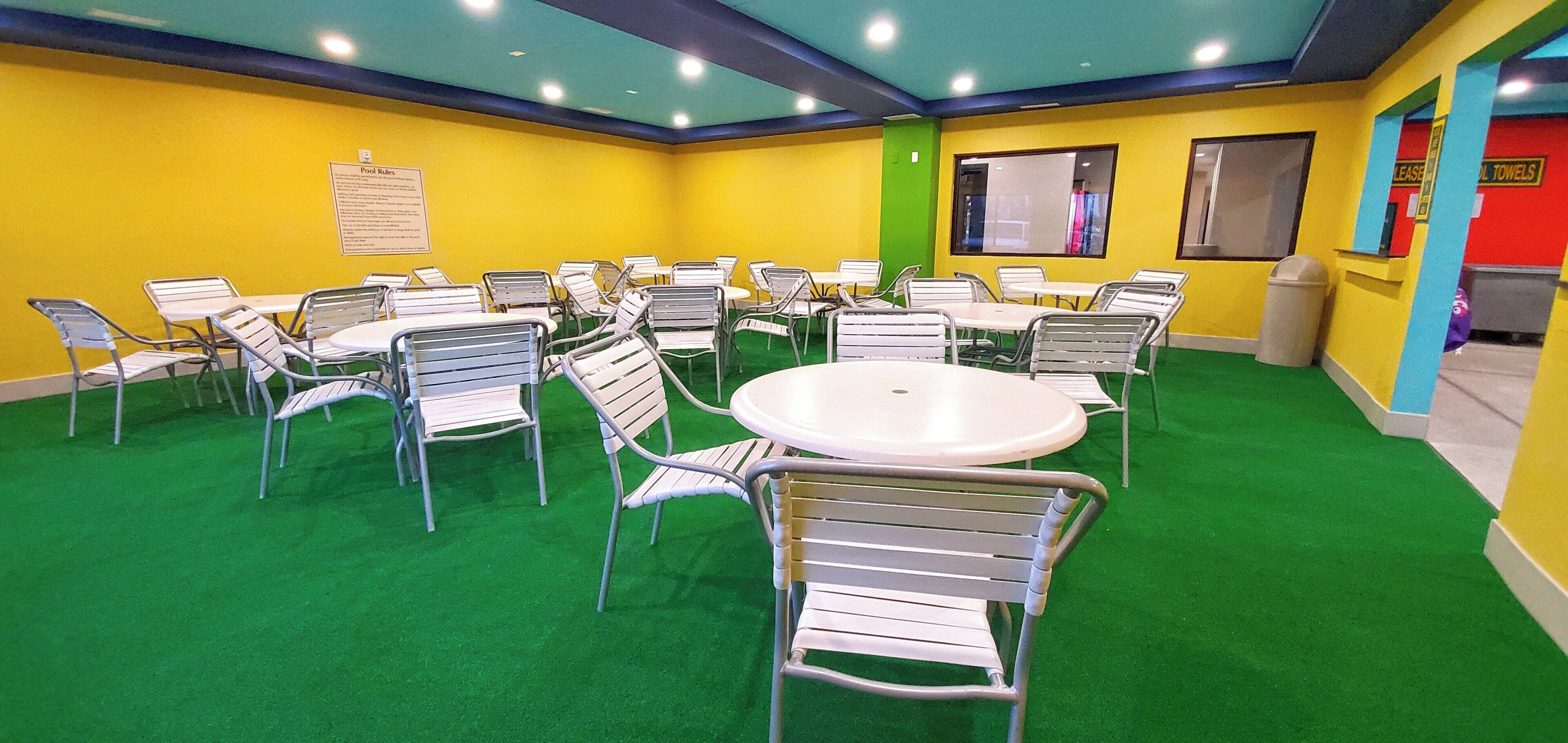A conference room with multiple tables and chairs, green carpet, and yellow walls.