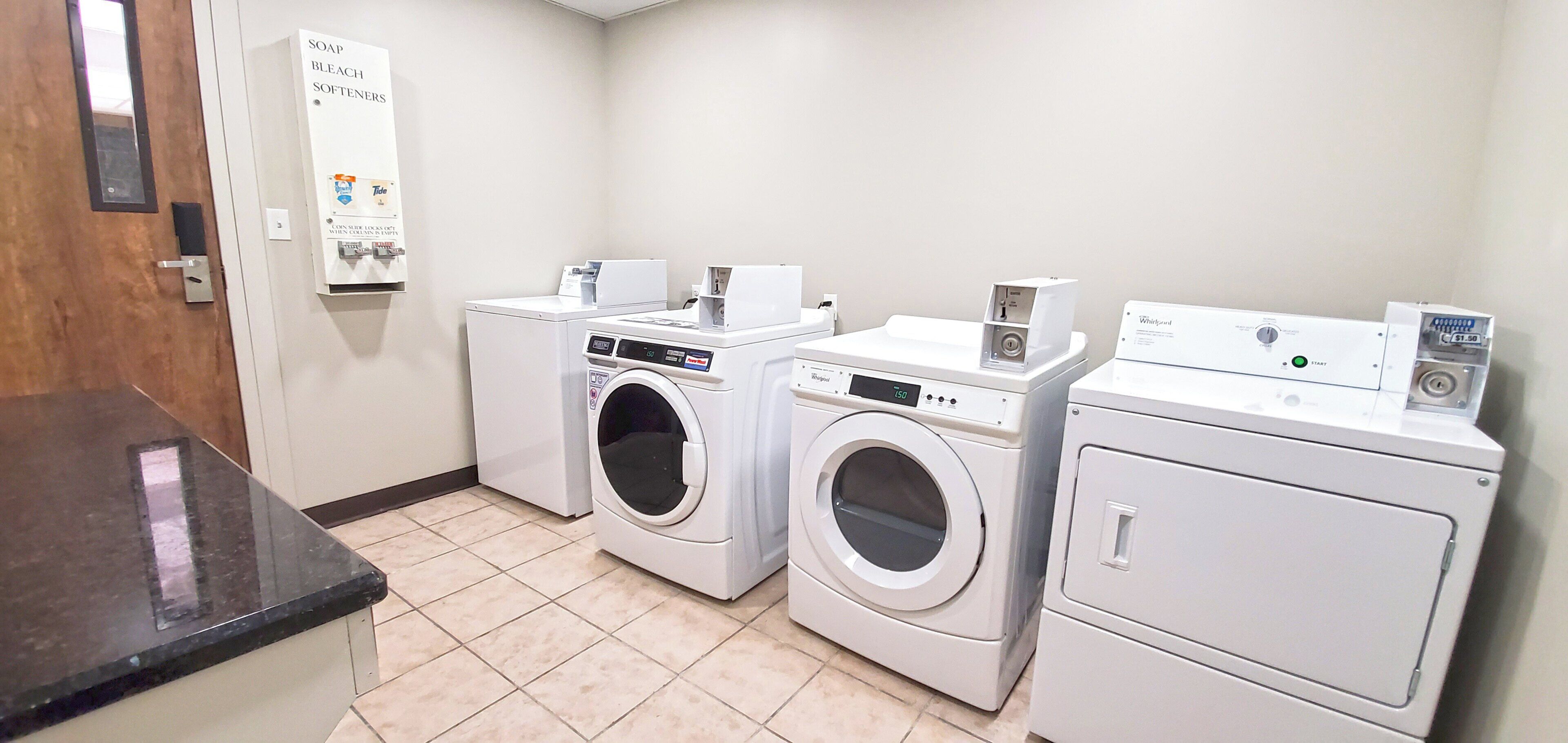 A laundry area with two front-loading washers and dryers, a soap and bleach dispenser, and a coin-operated dryer.