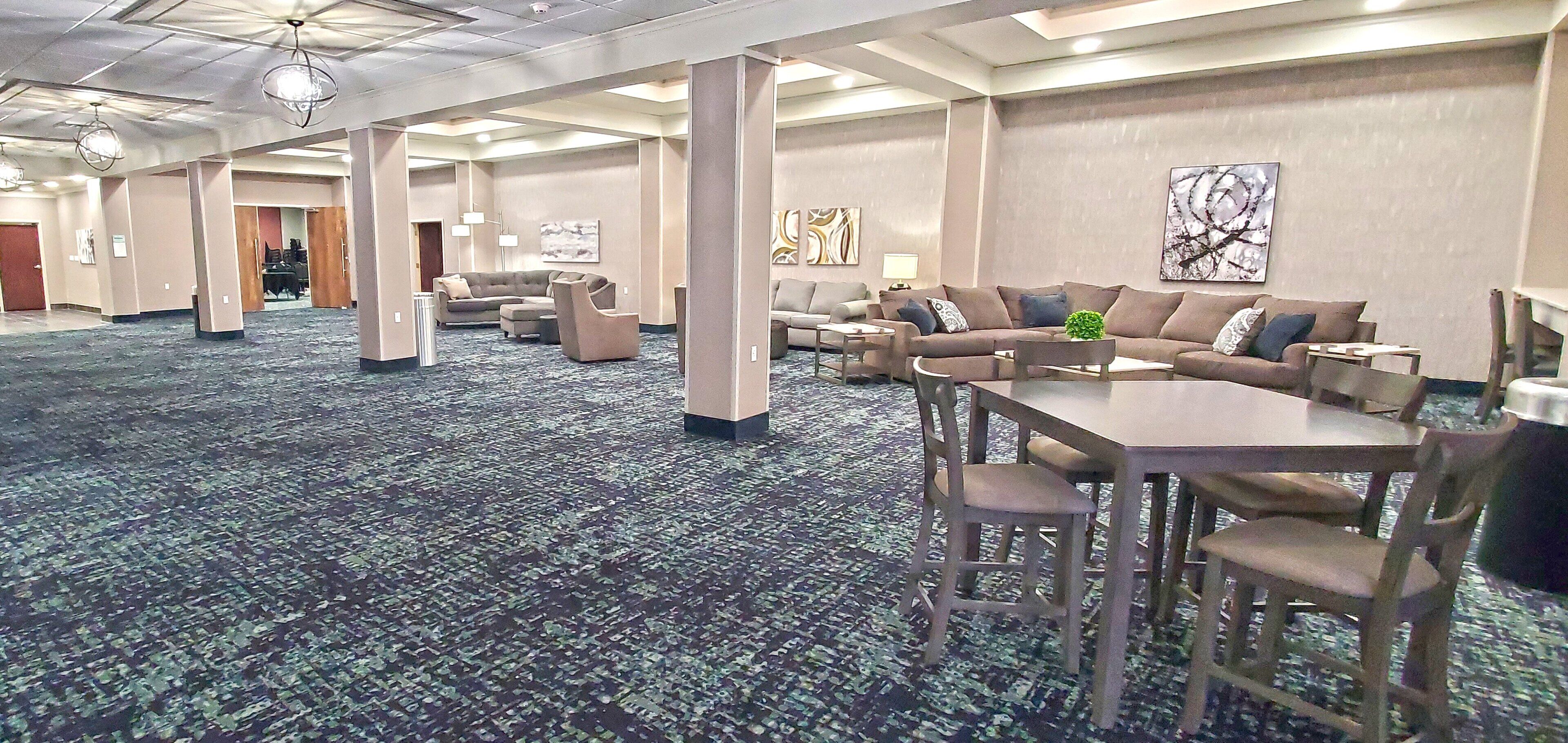 A spacious hotel lobby with multiple seating areas, including sofas and a dining table with chairs.