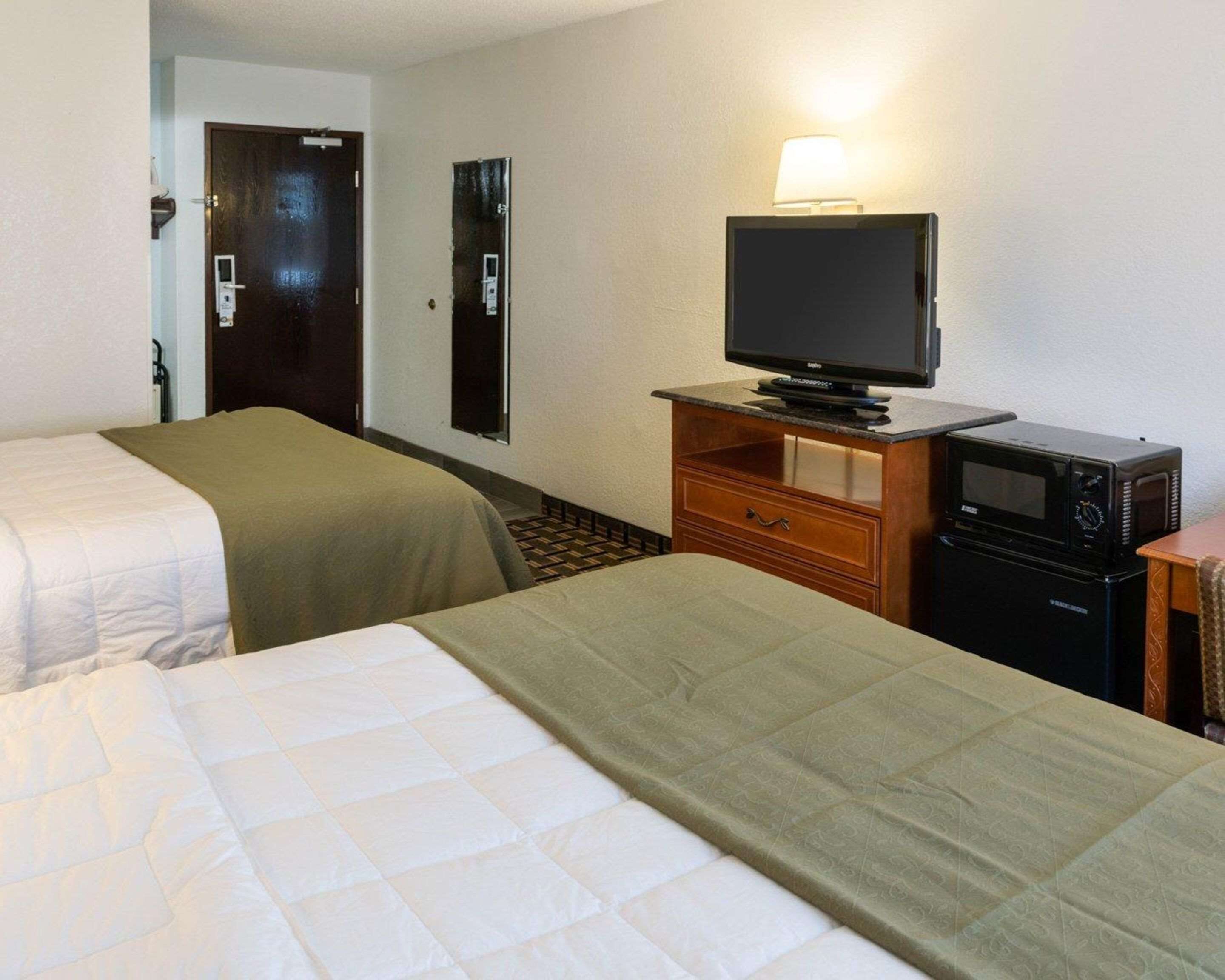 A hotel room with two beds, a television, a microwave, and a small wooden cabinet.