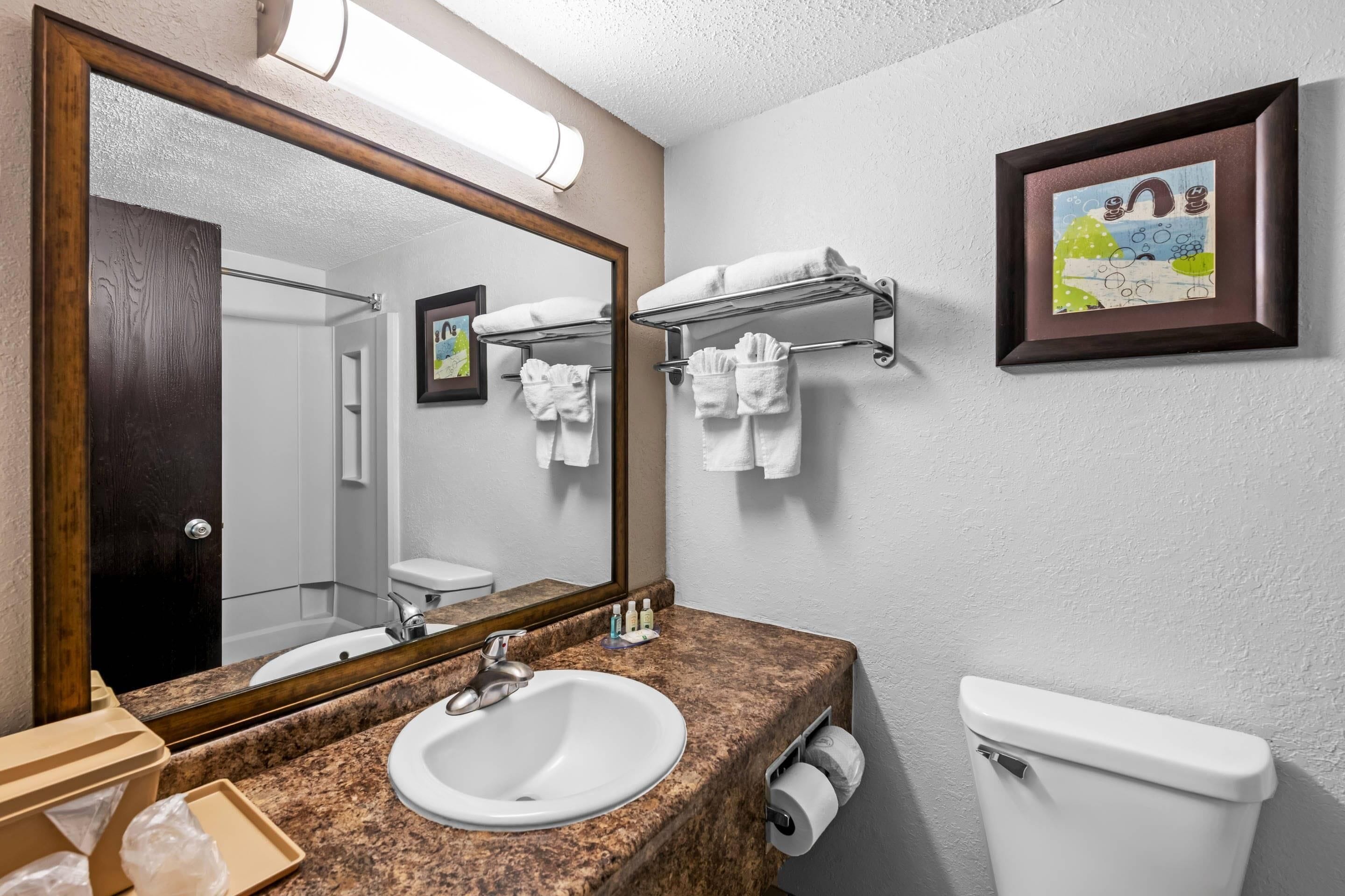 A bathroom with a granite countertop sink, a mirror, a towel rack, and a toilet.