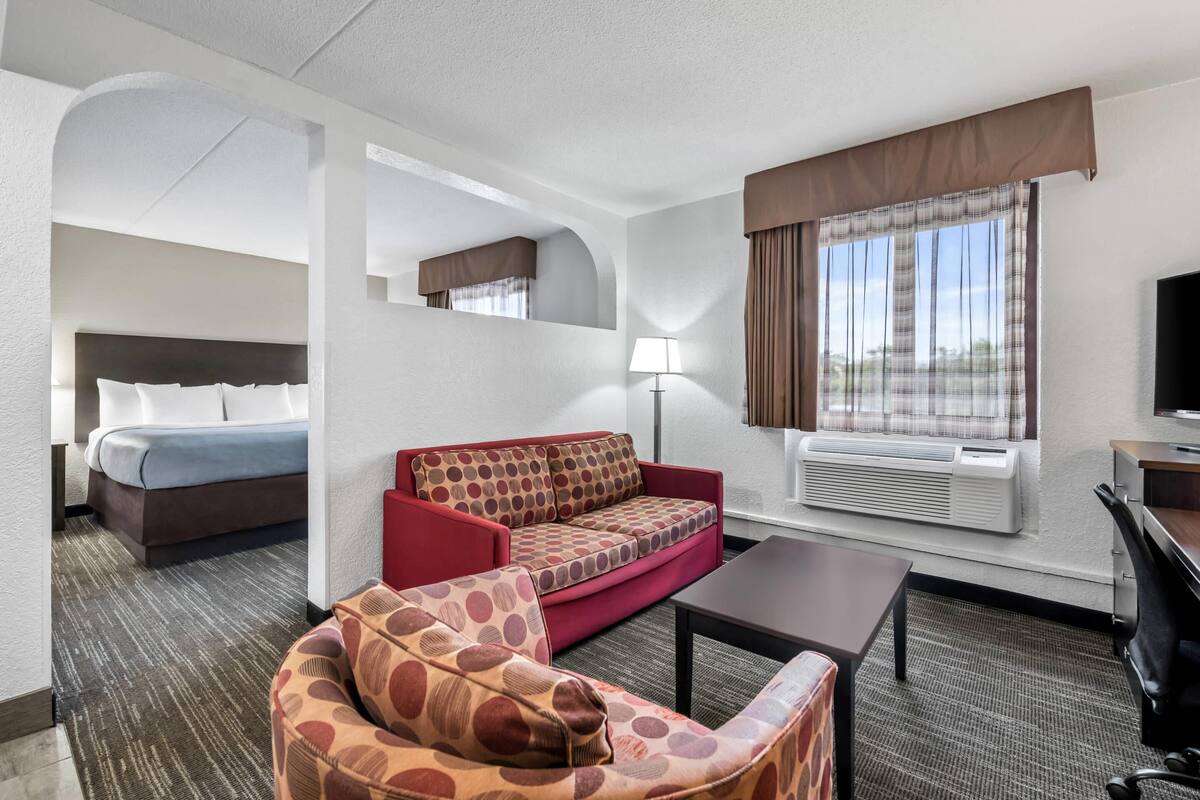 A hotel room with a bed, a red sofa, a small armchair, a desk, and a TV.
