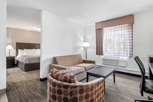 Habitación de hotel con cama, sofá, sillón, mesa y ventana con cortinas.