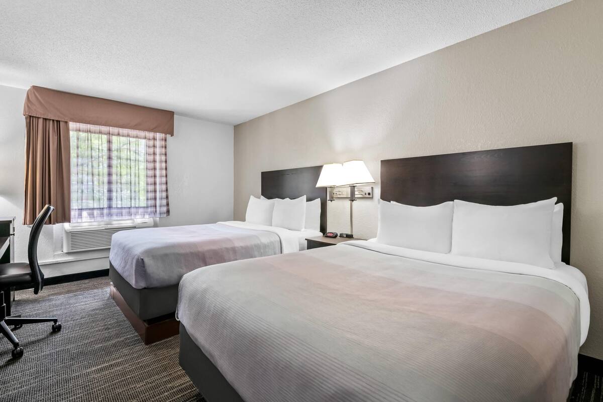 A hotel room with two beds, a desk, and a window with curtains.