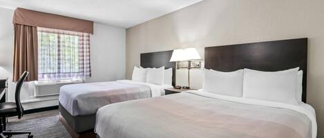 A hotel room with two beds, a desk, and a window with curtains.